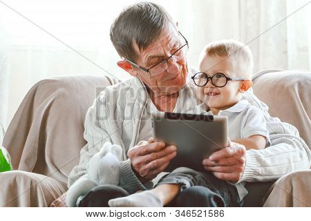Elderly Grandfather And His Little Grandson Use A Tablet Device