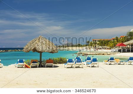 Beautiful View Of White Sand Curacao Beach. Blue Sunbeds Under Sun Umbrellas On Turquoise Water And 