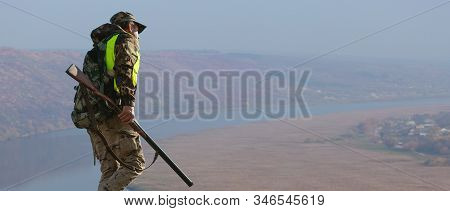 Hunter Man In Camouflage With A Gun During The Hunt In Search Of Wild Birds Or Game. Autumn Hunting 