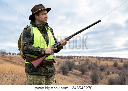 Hunter Man In Camouflage With A Gun During The Hunt In Search Of Wild Birds Or Game. Autumn Hunting 