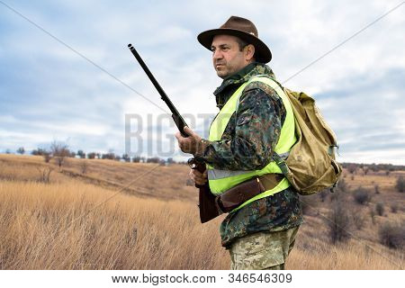 Hunter Man In Camouflage With A Gun During The Hunt In Search Of Wild Birds Or Game. Autumn Hunting 