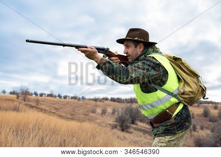 Hunter Man In Camouflage With A Gun During The Hunt In Search Of Wild Birds Or Game. Autumn Hunting 