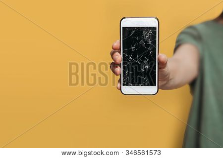 Close Up, Hand Holding Broken Smartphone With Cracked Cellphone Screen. Isolated On Yellow Backgroun