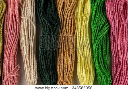 At The Top Of The Photo, Embroidery Threads Lie Vertically. They Have Various Color Shades.