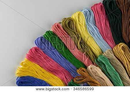 At The Top Of The Photo, Embroidery Threads Lie Vertically. They Have Various Color Shades.