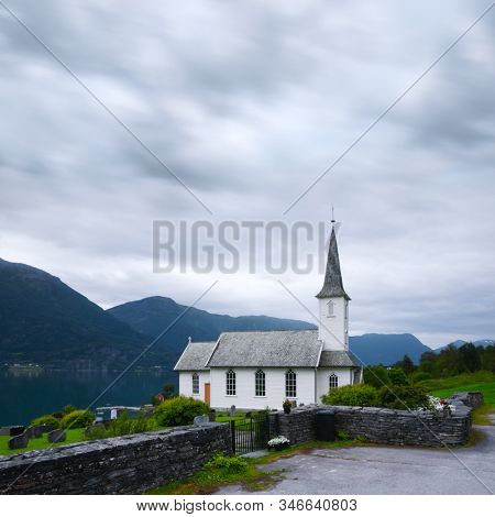 Typical christianity church with cemetery of Nes village, parish church in Luster Municipality in Sogn og Fjordane county, Norway. Lustrafjorden fjord on background. Landscape photography