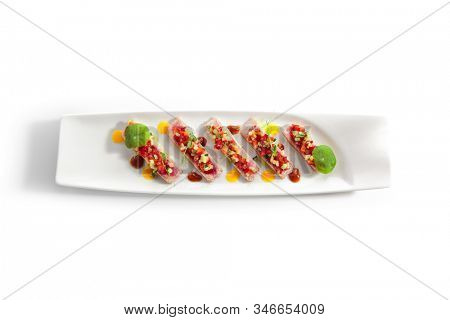 Appetizer with tuna tartar, seasonal vegetables and greens on white restaurant plate isolated. Macro photo of delicious healthy red fish tatar or tar-tar entree closeup