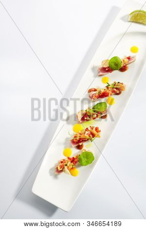 Appetizer with tuna tartar, seasonal vegetables and greens on white restaurant plate isolated. Macro photo of delicious healthy red fish tatar or tar-tar entree topview