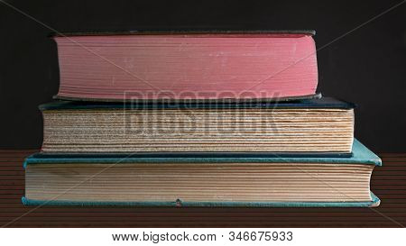 Closeup On The Fore Edge Of Three Old Books Stacked On Top Of Each Other, On Wooden Table, Against D