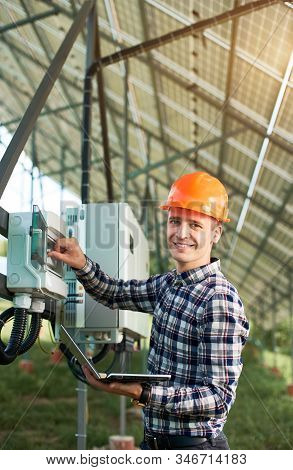 Smiling Woker In Helmet And With Laptop At Station Pushing Button At The Electrical Equipment On Sol
