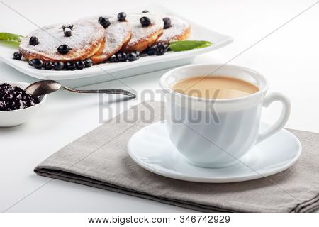 A Cup Of Coffee With Milk And A Plate With A Pancakes Is On The Table.