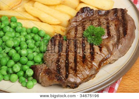 Bistecca di manzo alla griglia con patatine grosso e piselli.