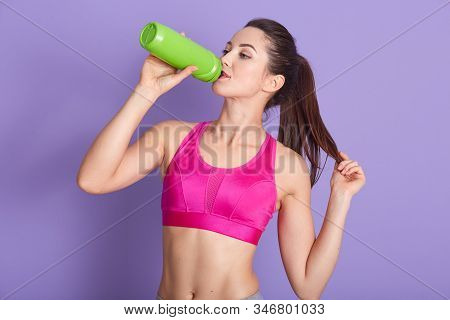 Profile Of Attractive Charmed Sporty Brunette With Ponytail Drinking Water From Green Bottle, Doing 