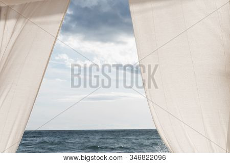 View Of The Sea Between White Curtains And White And Blue Clouds Sky