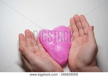 The Child's Hands Hold A Slime In The Form Of A Pink Heart. Concept. Valentine's Day.