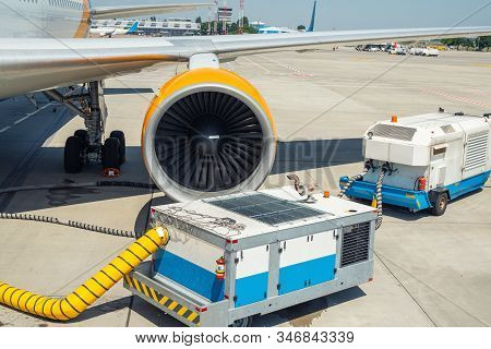 Big Modern Commercial Plane Parked On Airport Runway And Connected To Ground Supply Power Unit. Airc