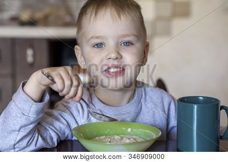 Cute Caucasian Baby Boy With Blue Eyes And Blond Hairs Eating Porridge. Smiling Pretty Face, Childre