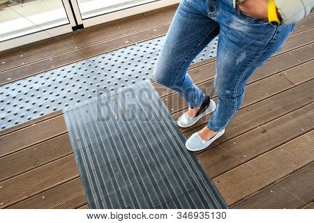 Female Legs In Denim Jeans Pants And Light Summer Sneakers Standing On Wooden Floow.