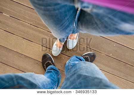 Top Down View Of Legs In Denim Jeans Pants And Light Summer Sneakers Standing On Wooden Floow.