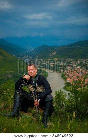 A Man In The National Costume Of Georgia Against The Backdrop Of The Mountains.