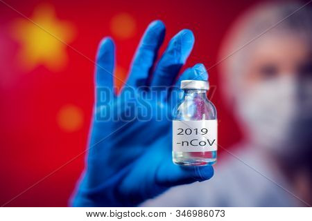A Doctor In Blue Medical Gloves And Mask Holding An Ampula With Vaccine In Front Of Flag Of China. C
