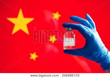 A Doctor In Blue Medical Gloves Holding An Ampula With Vaccine In Front Of Flag Of China. Close Up S