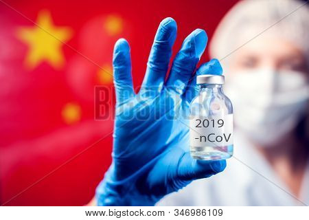A Doctor In Blue Medical Gloves And Mask Holding An Ampula With Vaccine In Front Of Flag Of China. C