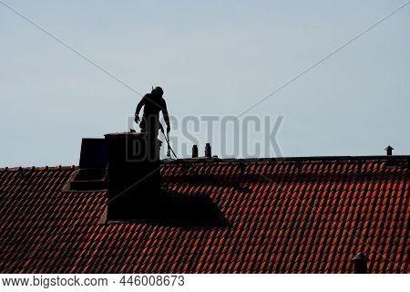 Silhouette Of A Chimney Sweeper On Top Of A Roof.