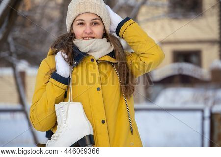 Portrait Of Young Woman In Yellow Jacket With Ice Skates Goes To Rink.