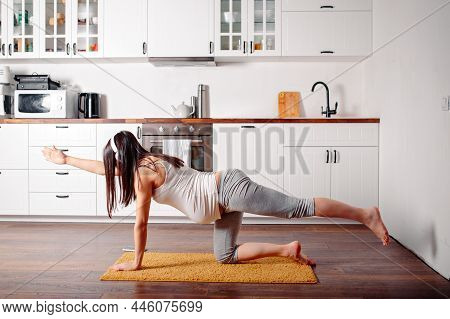 Pregnant Doing Workout On Orange Fitness Mat. Pragnant Yoga At Home In The Kitchen. Pregnant In Whit