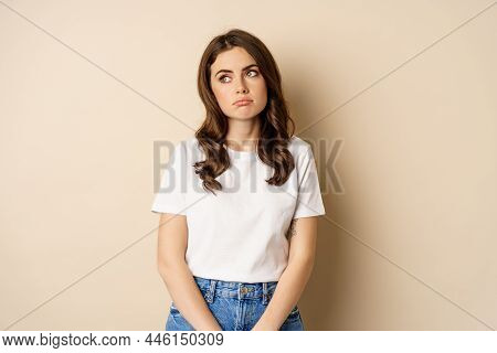 Sad And Tired Brunette Woman Looking Drained And Unamused, Standing With Pokerface Against Beige Bac