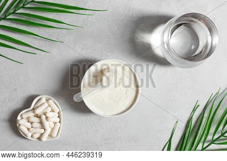Collagen Powder In A Bowl, Collagen Capsules And A Glass Of Water On A Gray Background With Palm Lea