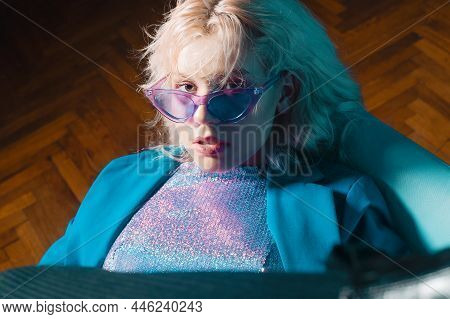 The Girl Is Like In The Clip From The 80s 90s. Short Blonde Haircut. The Girl Is Sitting On A Chair 