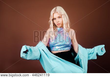 A Blonde In A Turquoise Jacket, In A Blue Jacket In Sequins, Poses In The Studio On A Brown Backgrou