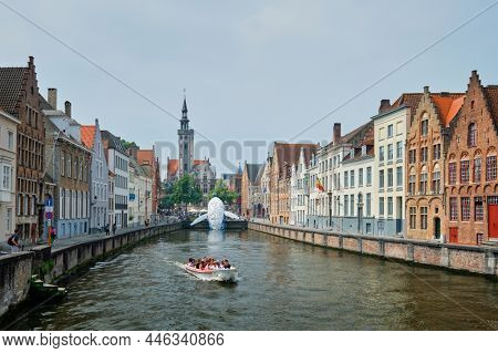 BRUGES, BELGIUM - MAY 29, 2018: Tourist boat in canal between old houses with The Bruges Whale plastic installation and The Burghers' Lodge Poortersloge tower. Brugge Bruges, Belgium