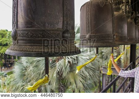 Black Metallic Bells Hanging In A Row Outside In Buddhist Temple. Hand Pulls The Yellow Ribbon Of A 