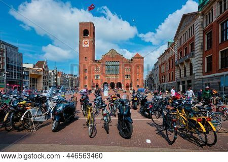Amsterdam, Netherlands - May 7, 2017: Beursplein with parked bicycles and motorcycles and Beurs van Berlage building - former commodity exchange building now venue for concerts exhibitions conferences