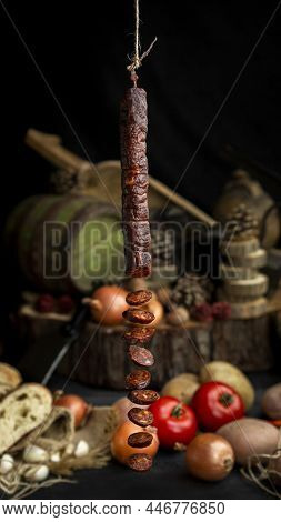 Smoked, Aged Sausage Hanging In The Kitchen With Fresh Vegetables And Food Ingrediets In The Backgro