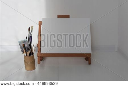 Empty copy space canwas on wood easel and paintbrush in artistic workshop interior