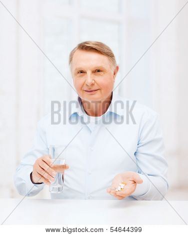 healthcare, madicine, pharmacy and elderly concept - old man with pills and glass of water