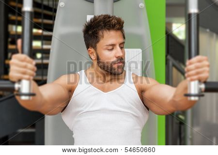 A handsome young muscular sports man doing butterfly exercise