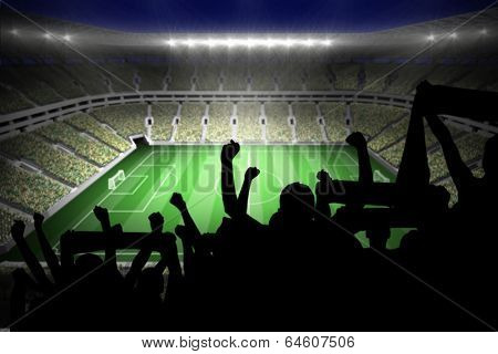 Silhouettes of football supporters against large football stadium with lights
