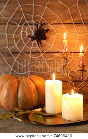 Halloween decoration with spider on web, pumpkin and candles on wooden background