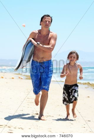 Jeune père et fils le long de la plage avec planche de surf