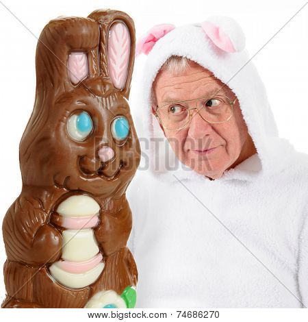 A giant chocolate bunny and a senior-man bunny eying each other as if vying for top spot on the Easter bunny scene.  On a white background.