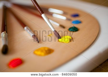 Paints On Wooden Pallet. Focus On Paintbrush Dipped In Yellow Paint