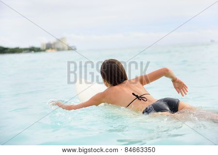 Surfer girl surfing paddeling on surfboard. Female surf bikini woman living healthy active water sports lifestyle on Hawaiian beach. Asian Caucasian model on Waikiki Beach, Oahu, Hawaii.