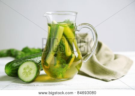 Glass ewer with fresh organic cucumber water on wooden table, on grey background