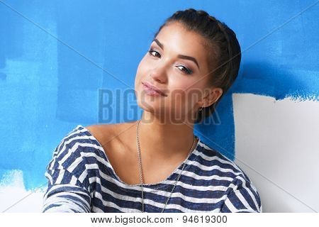 Beautiful young woman doing wall painting, standing near ladder