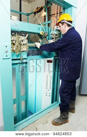male technician machinist worker adjusting elevator mechanism of lift with spanner